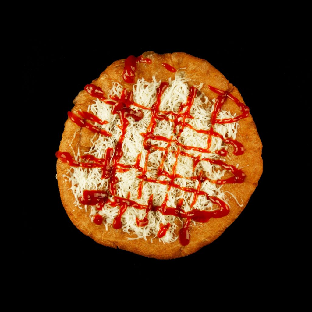 Appetizing Hungarian lángos topped with shredded cheese and sauce on a black background.